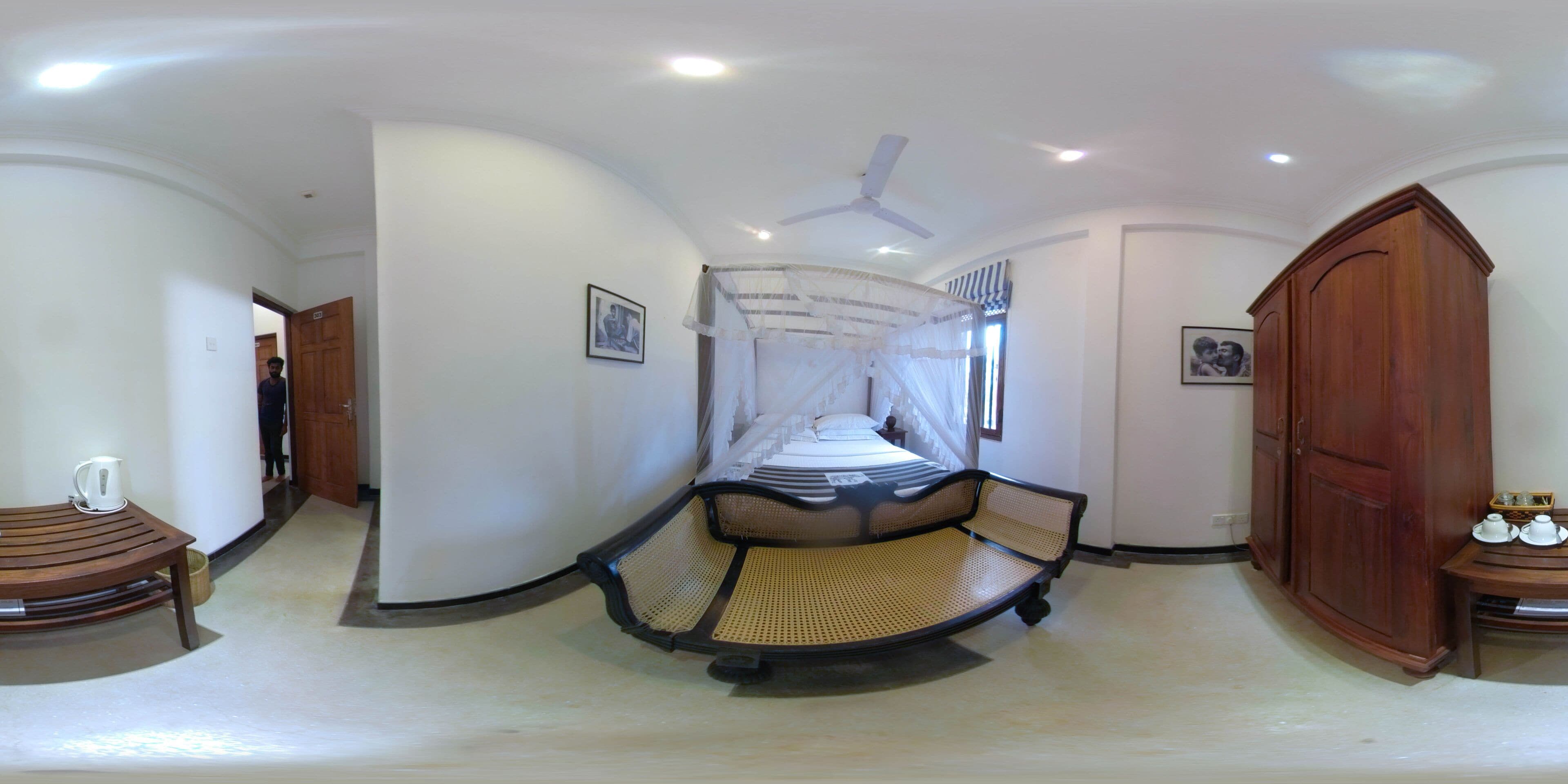 A bedroom with a canopy bed, a wooden wardrobe, and a small table with a pitcher.