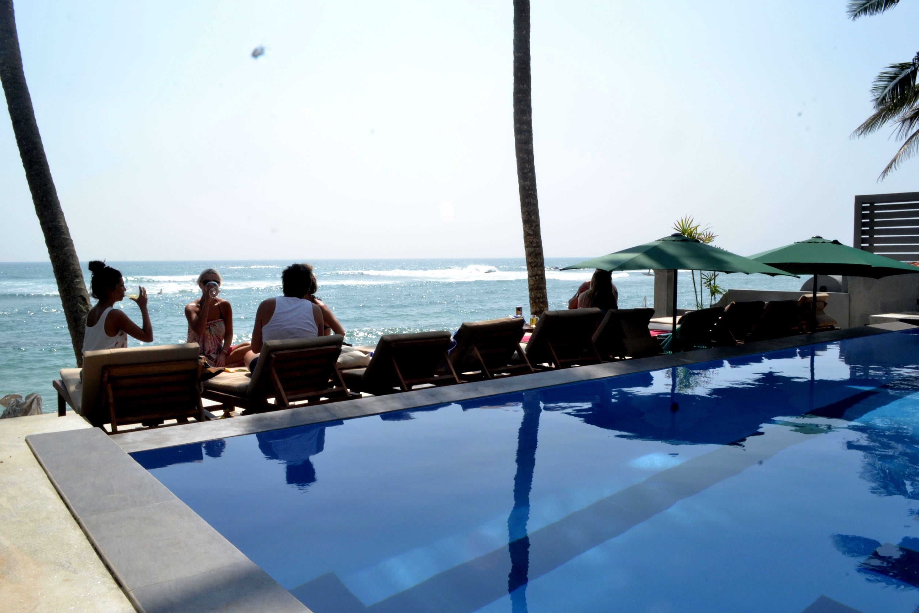 A poolside area with lounge chairs and umbrellas, overlooking the ocean.
