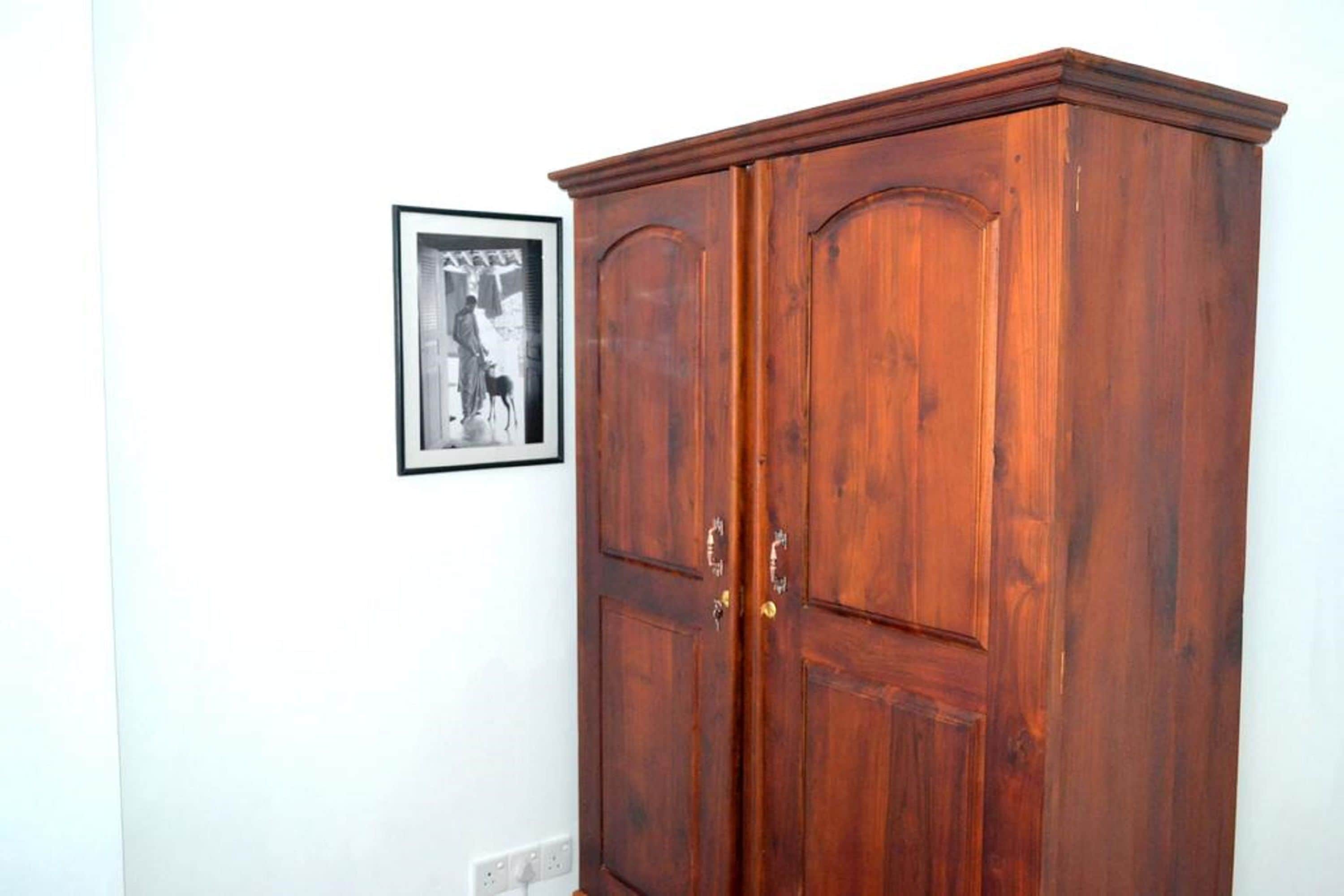 A wooden wardrobe with two doors and a small framed picture on the wall.