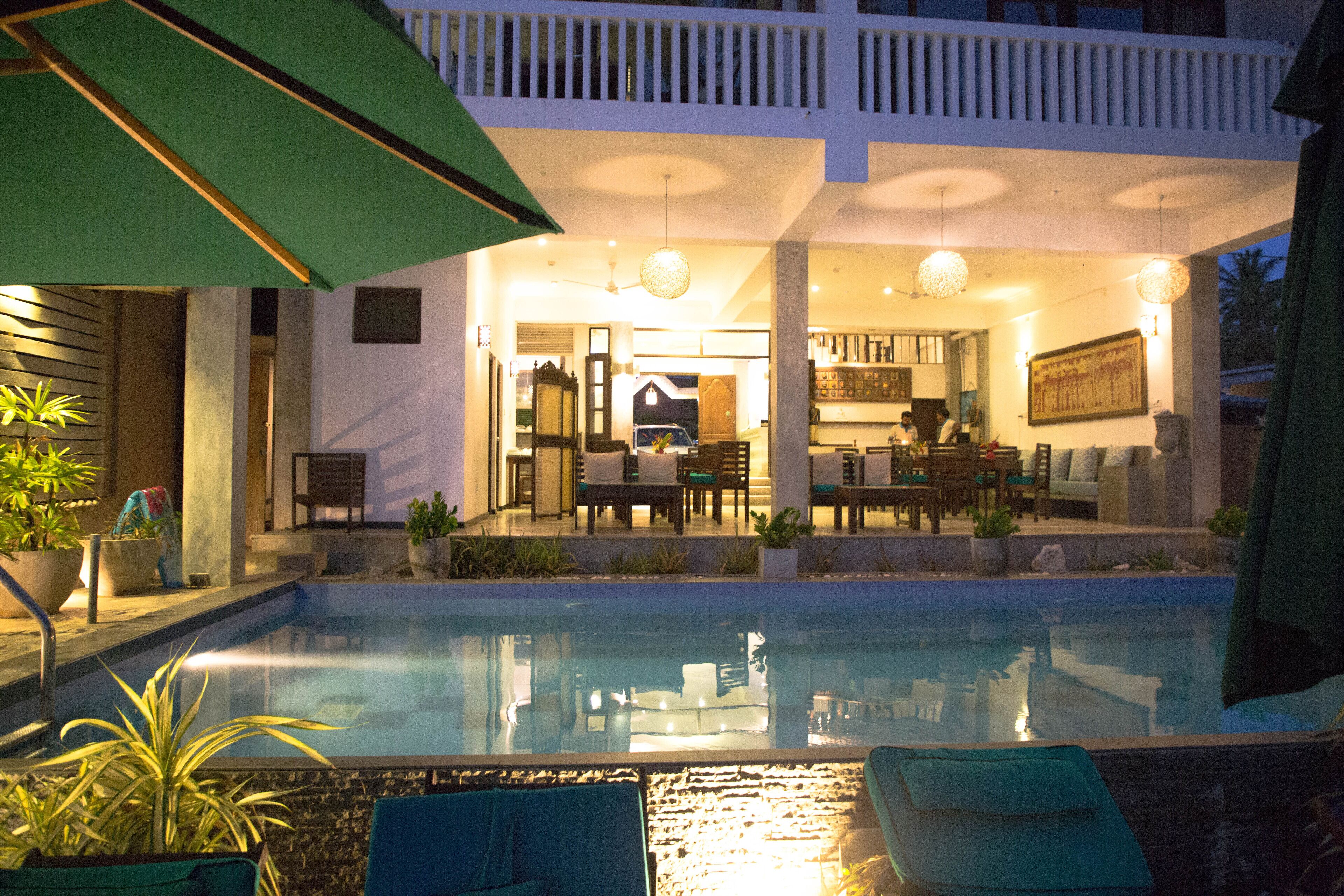 A pool area with lounge chairs, a dining area, and a kitchen visible through an open door.