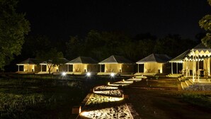 A series of illuminated tents with a pathway leading to them, surrounded by trees and a body of water. - Rangiri Dambulla Resort (Dambulla)
