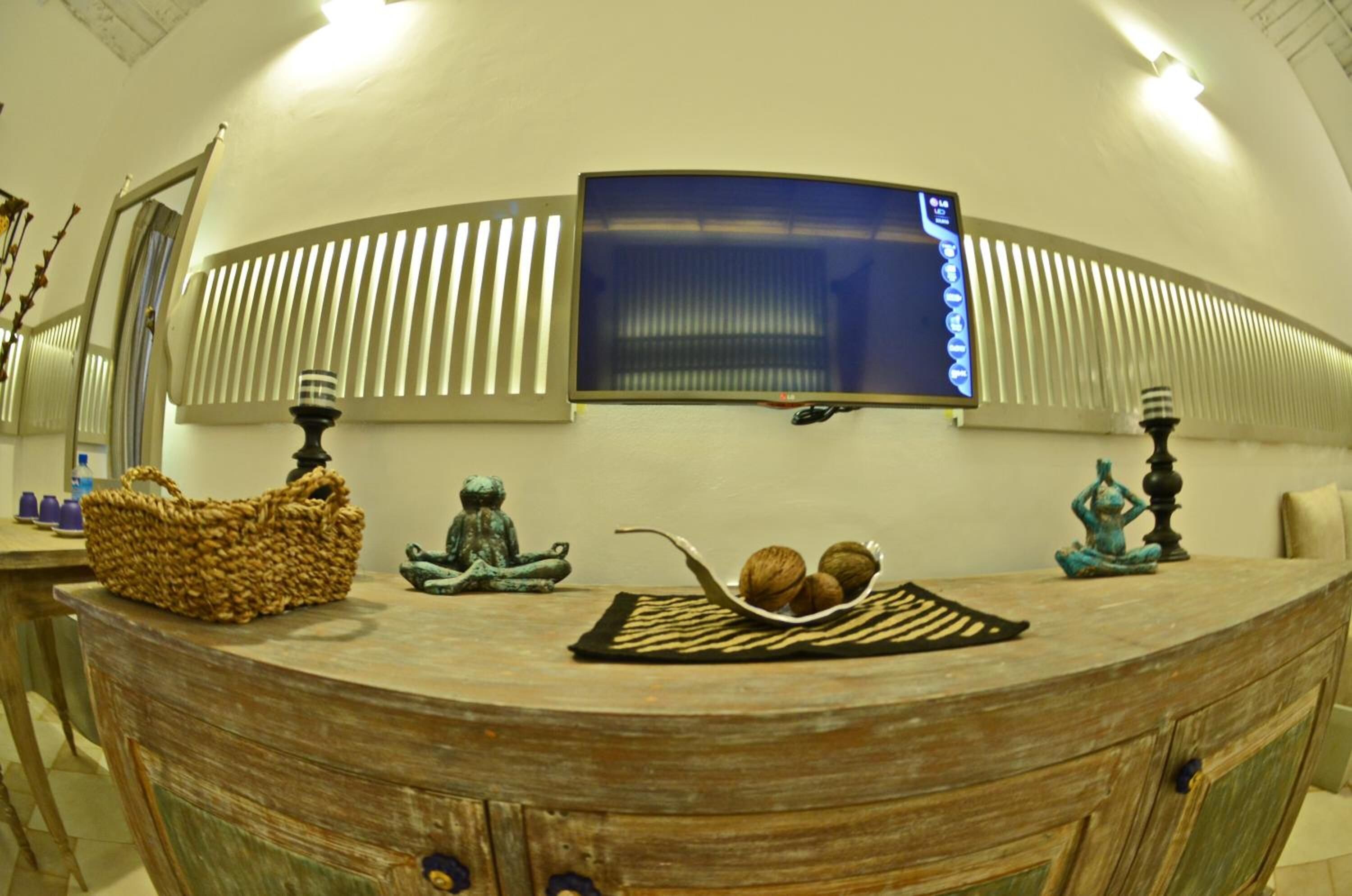Un mostrador de recepción curvo de madera con una cesta tejida, una pequeña estatua y una bandeja con nueces. Un televisor de pantalla plana está montado en la pared sobre el mostrador.