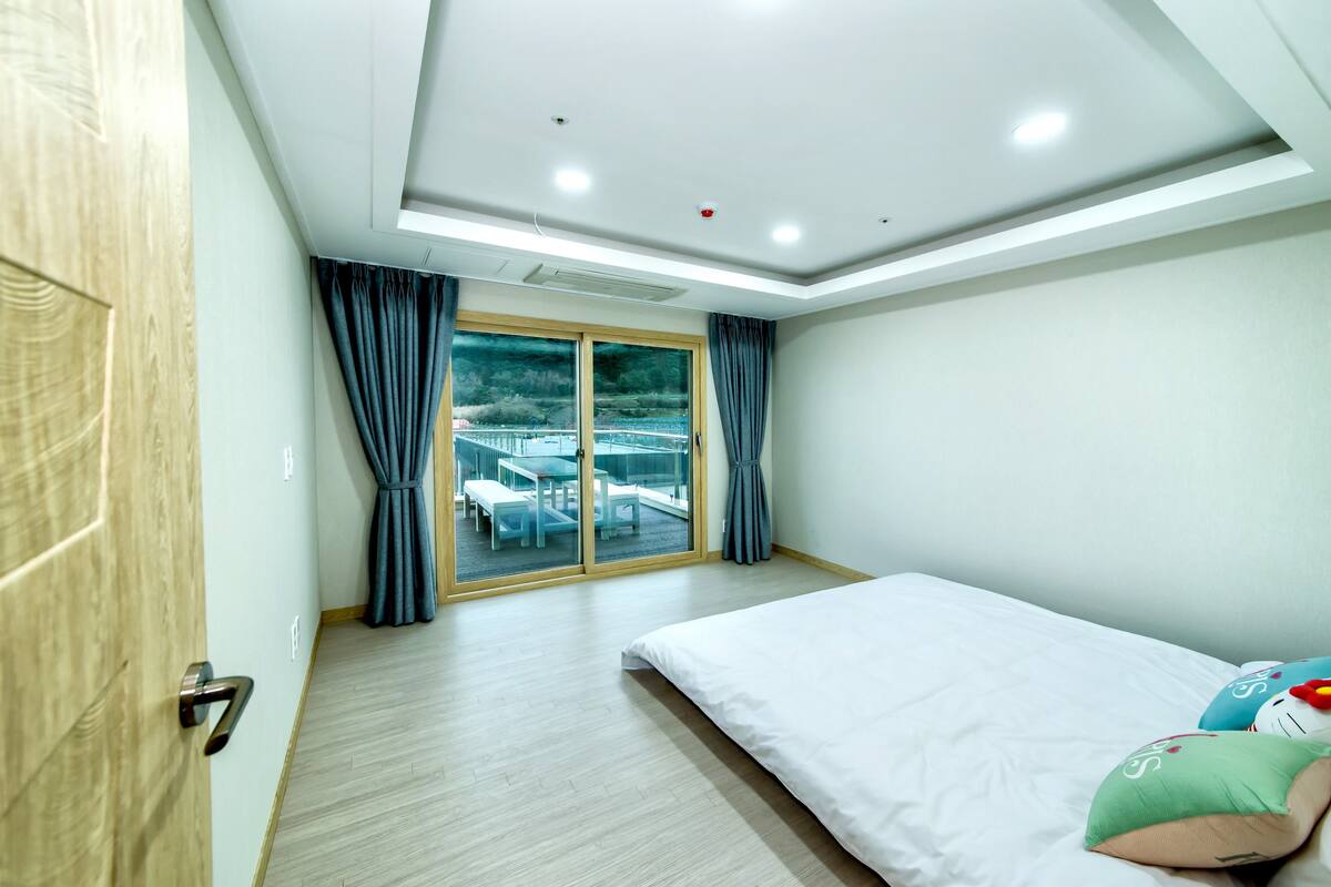 A modern hotel room with a large bed, a sliding glass door to a balcony, and a view of the cityscape.