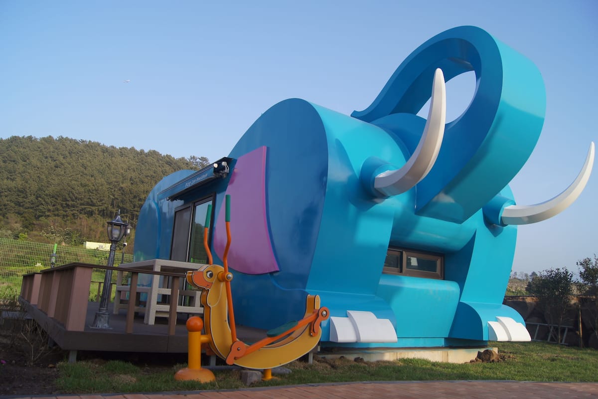 A large blue and white elephant sculpture with a swing seat and a small platform with a lamp.