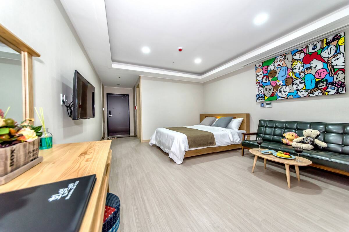 A modern hotel room with a bed, a sofa, a dining table, and a large wall mural.