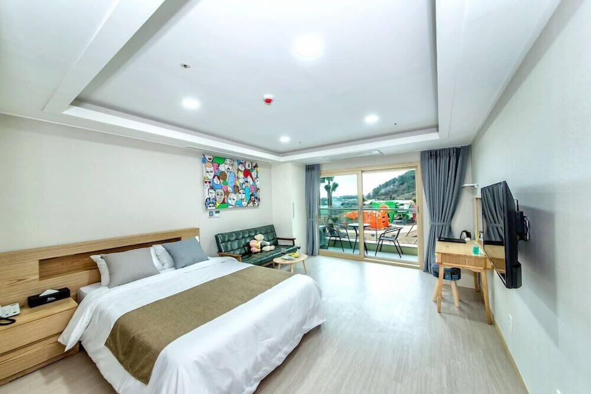 A hotel room with a bed, a desk, a chair, a television, and a balcony with a view.