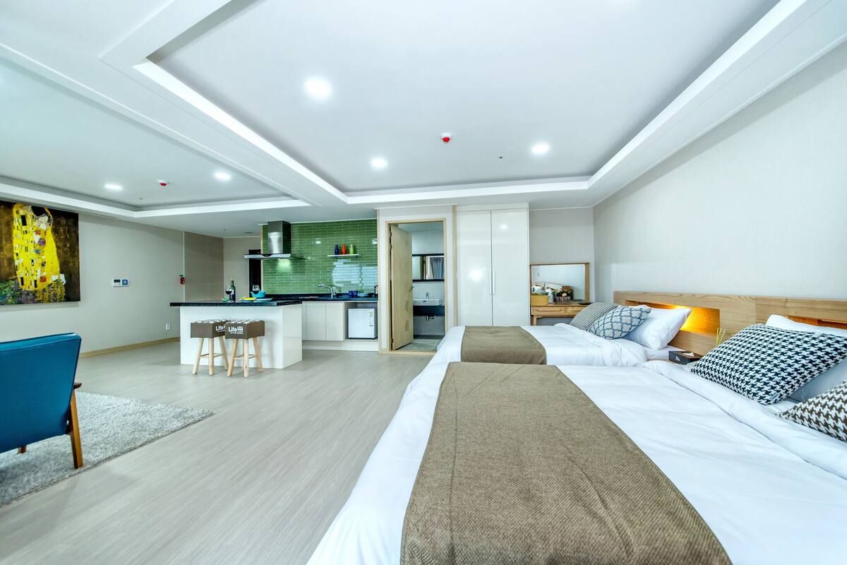 A modern hotel room with a large bed, a desk, and a kitchenette.