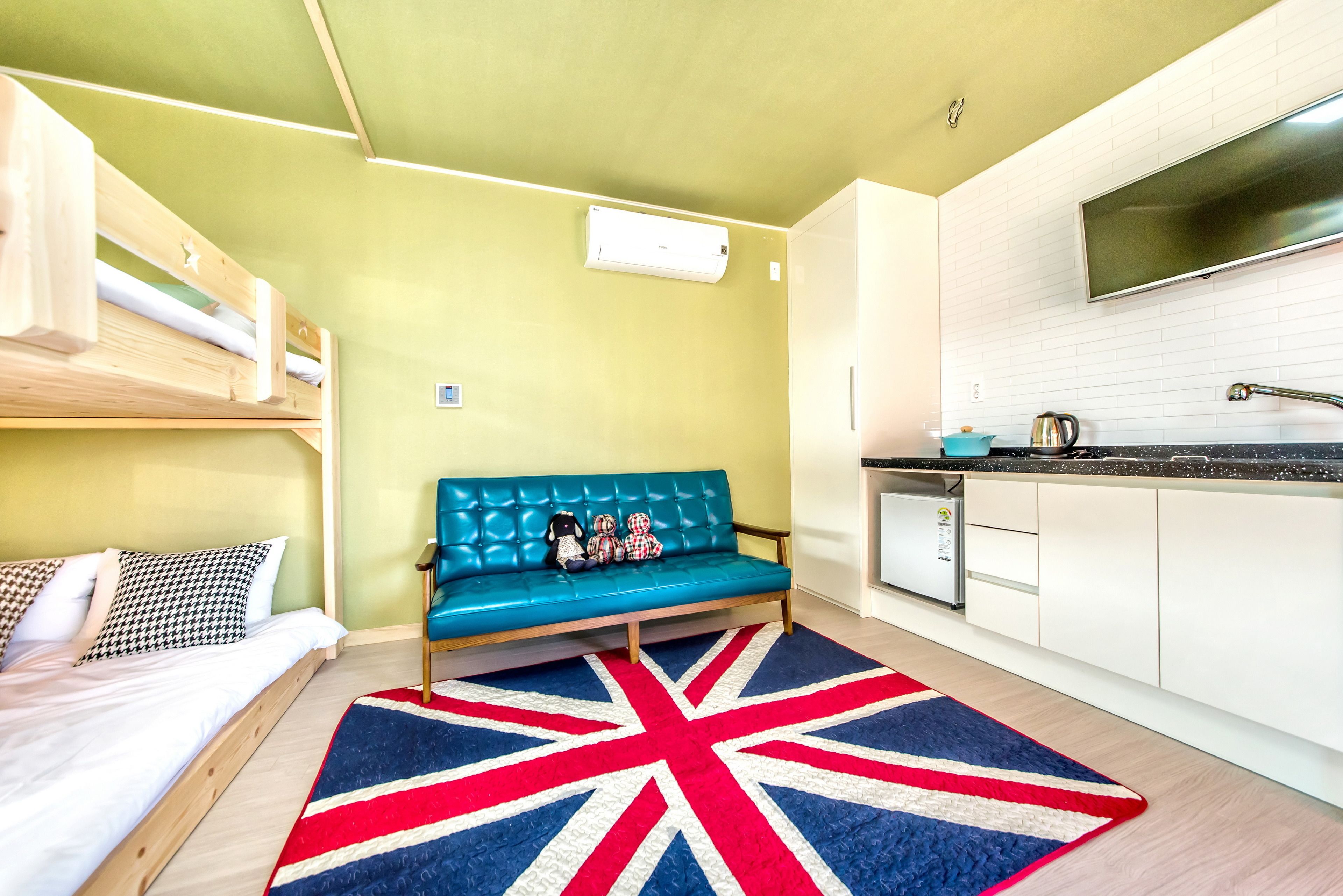 A compact room with a bunk bed, a sofa with toys, a kitchen area, and a Union Jack rug.