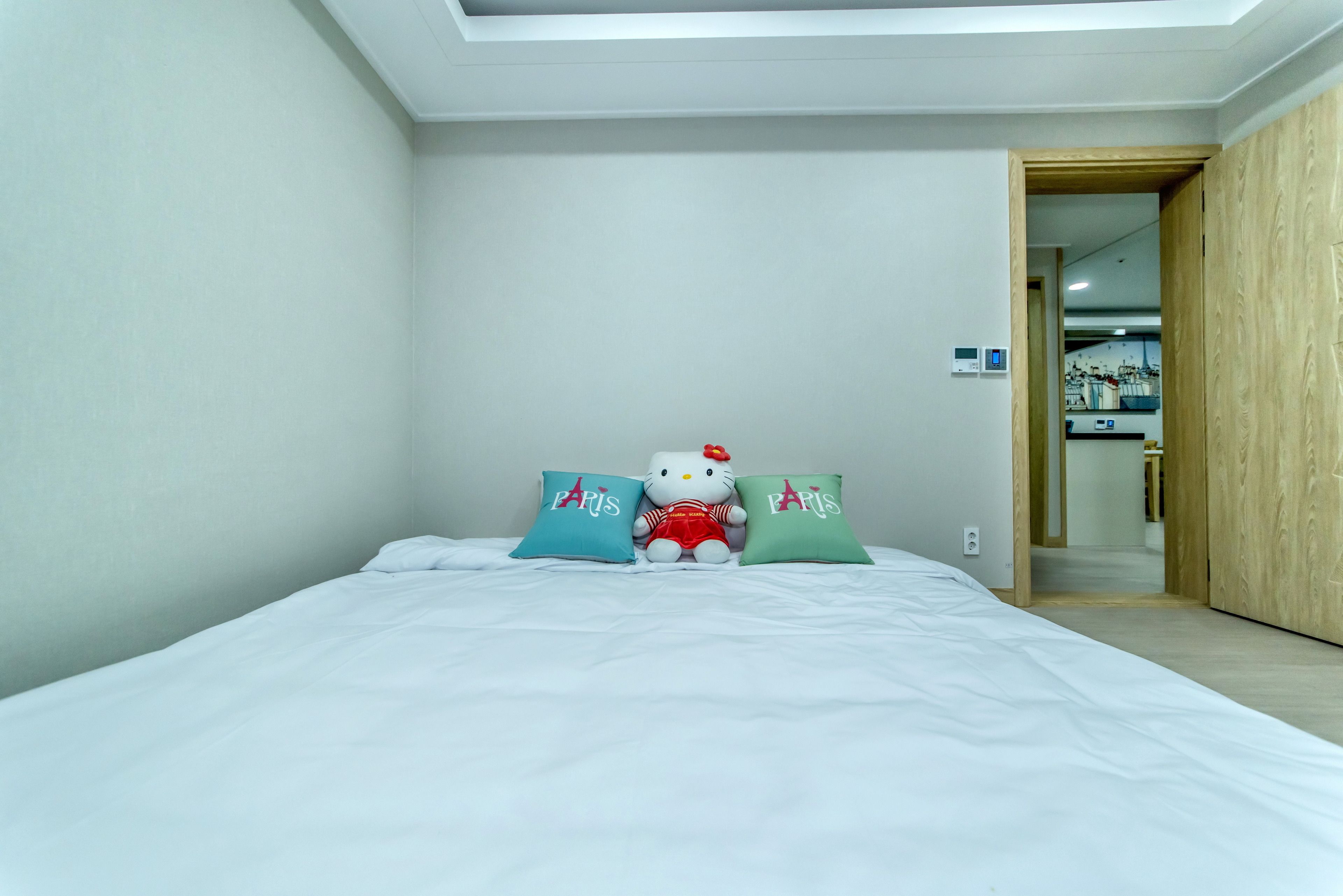 A bedroom with a bed, two pillows with 'Paris' text, and a Hello Kitty plush toy.