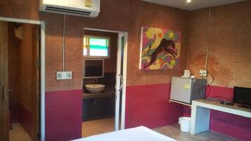 A hotel room with a bed, a desk with a computer, a sink, and a painting on the wall.