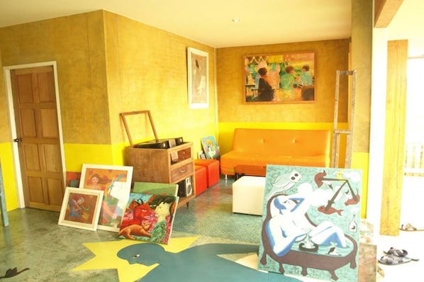 A room with a yellow wall, a wooden door, a sofa, and a table with framed artwork.
