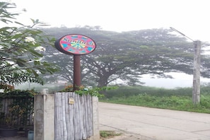A sign for Sundara, a guesthouse, with a bamboo fence and a road in the background.