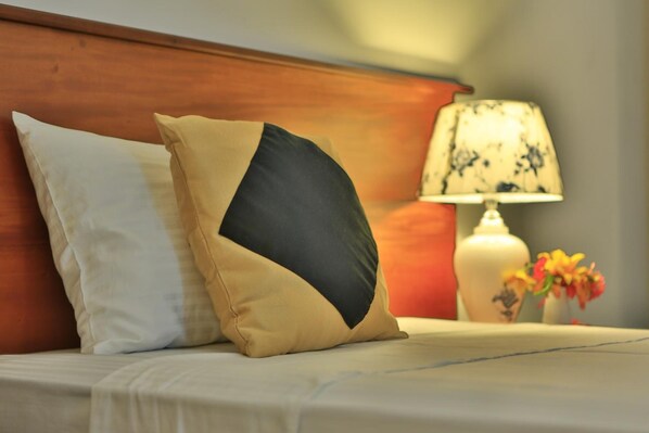 Una cama con dos almohadas, una mesita de noche con una lámpara y un florero con flores.