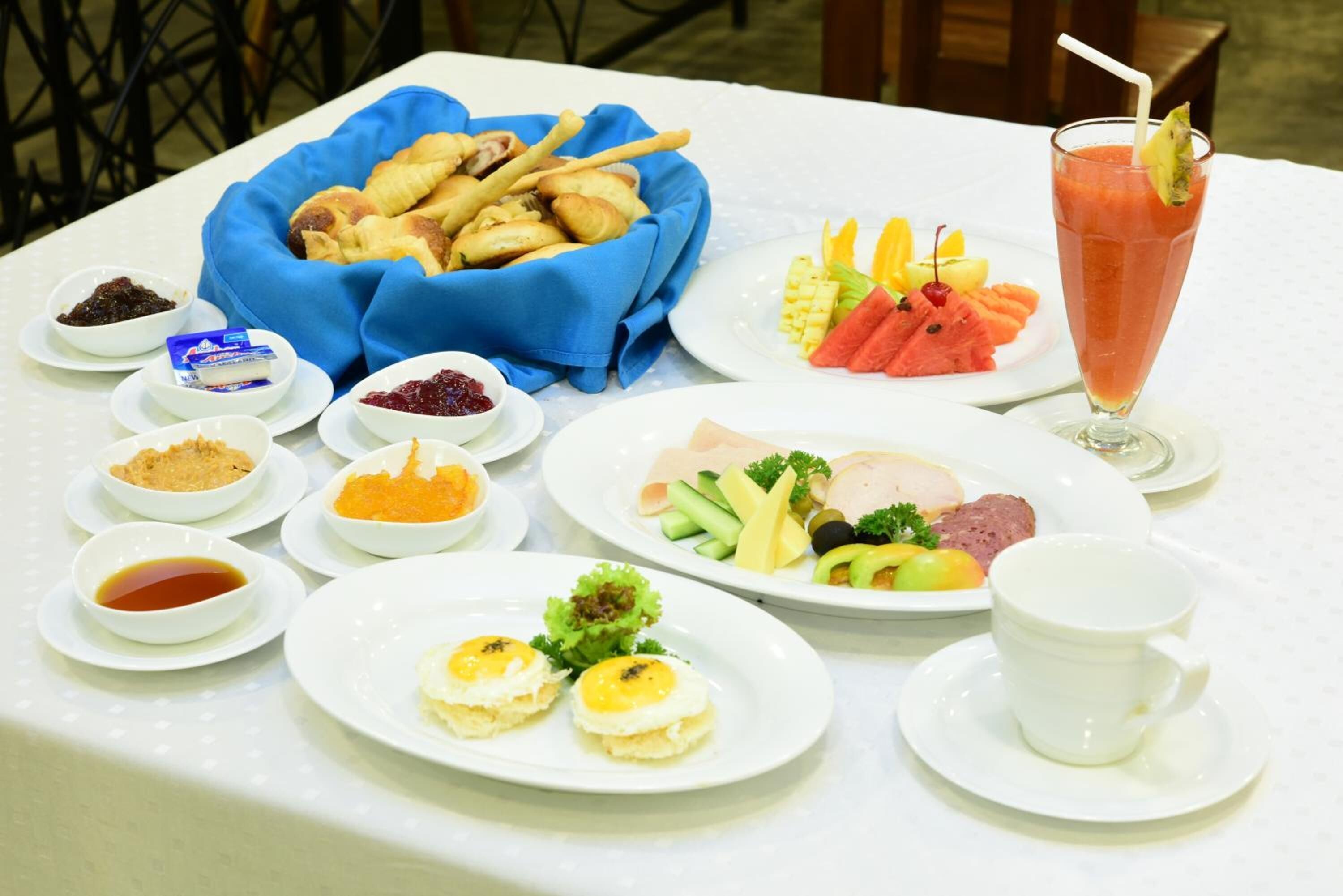 A table set with various dishes including bread, fruits, eggs, and a drink.