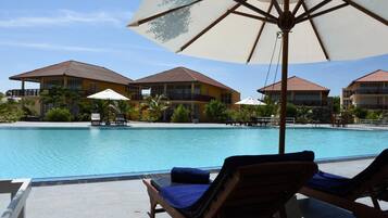 A pool area with lounge chairs and umbrellas, surrounded by buildings with balconies.