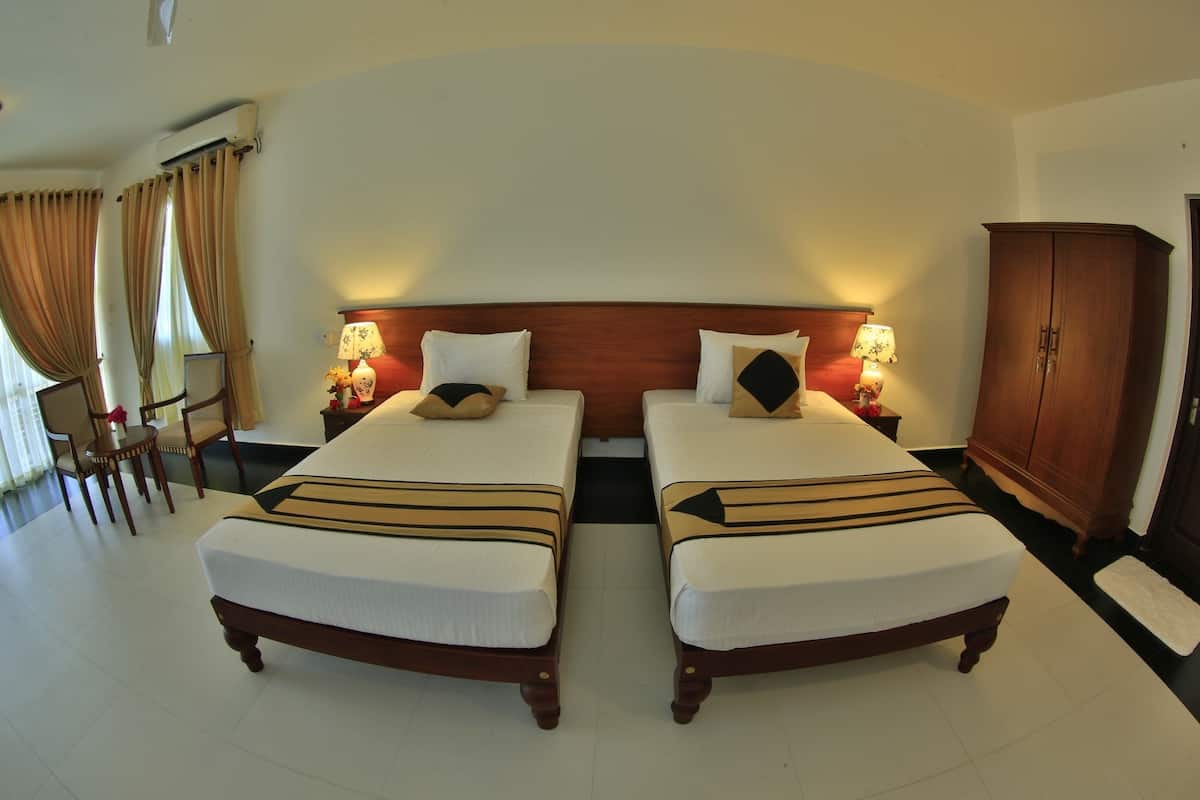 A hotel room with two beds, a wooden wardrobe, a desk with a chair, and a window with curtains.