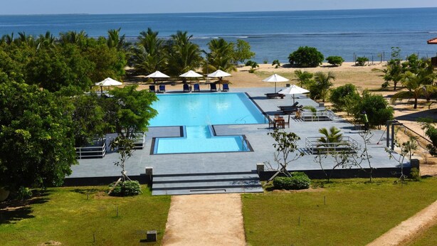 A pool area with a view of the ocean, surrounded by palm trees and lounge chairs. - Passi Villas Passikudah (Pasikuda)