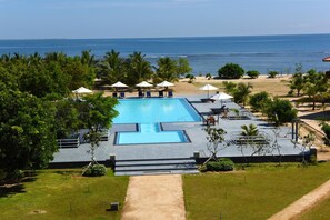 Zona de piscina con vista al océano, rodeada de palmeras y sillones de descanso.