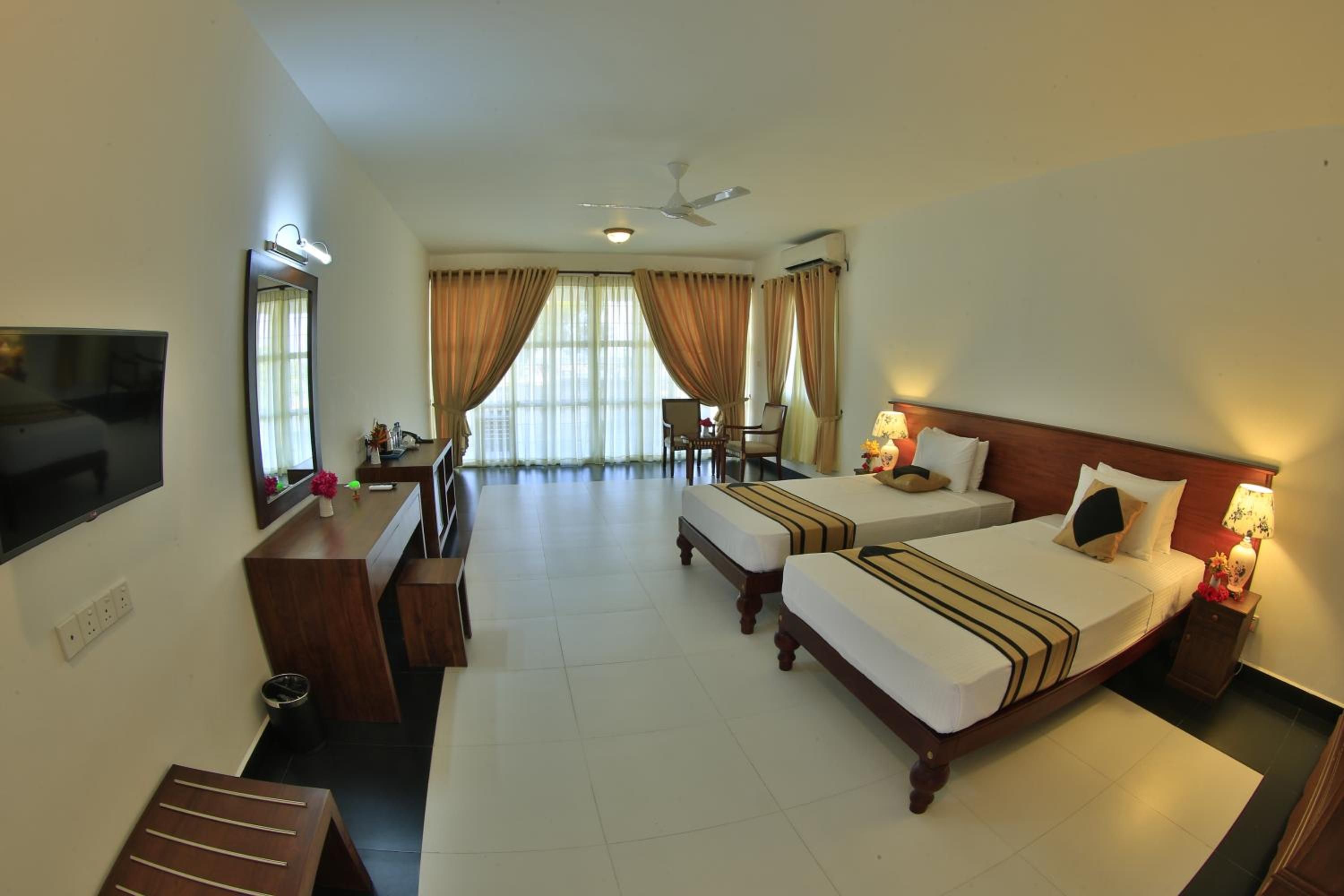 A hotel room with two beds, a desk, a TV, and a ceiling fan.