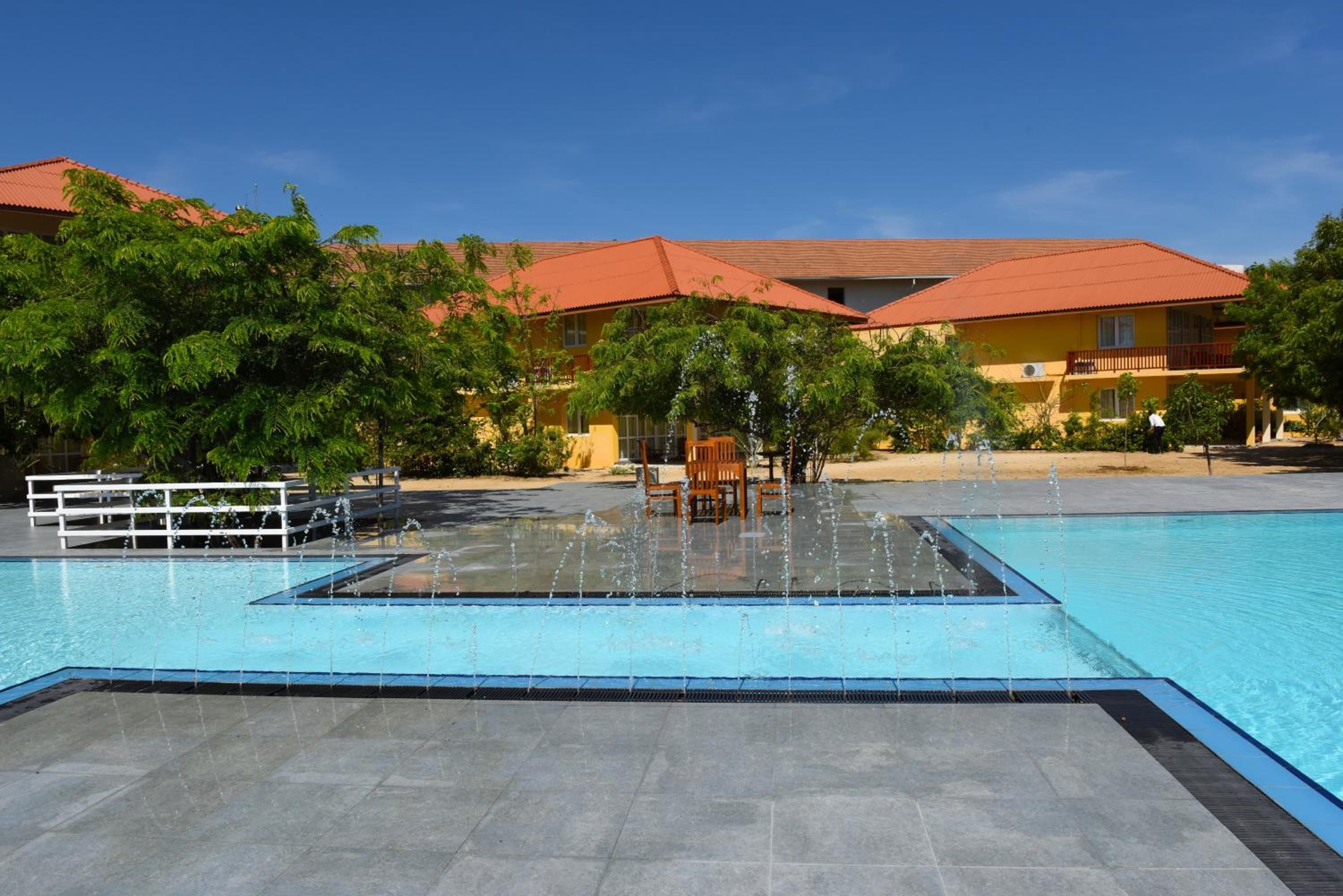 A swimming pool with a fountain feature, surrounded by a building with red-tiled roofs and greenery.