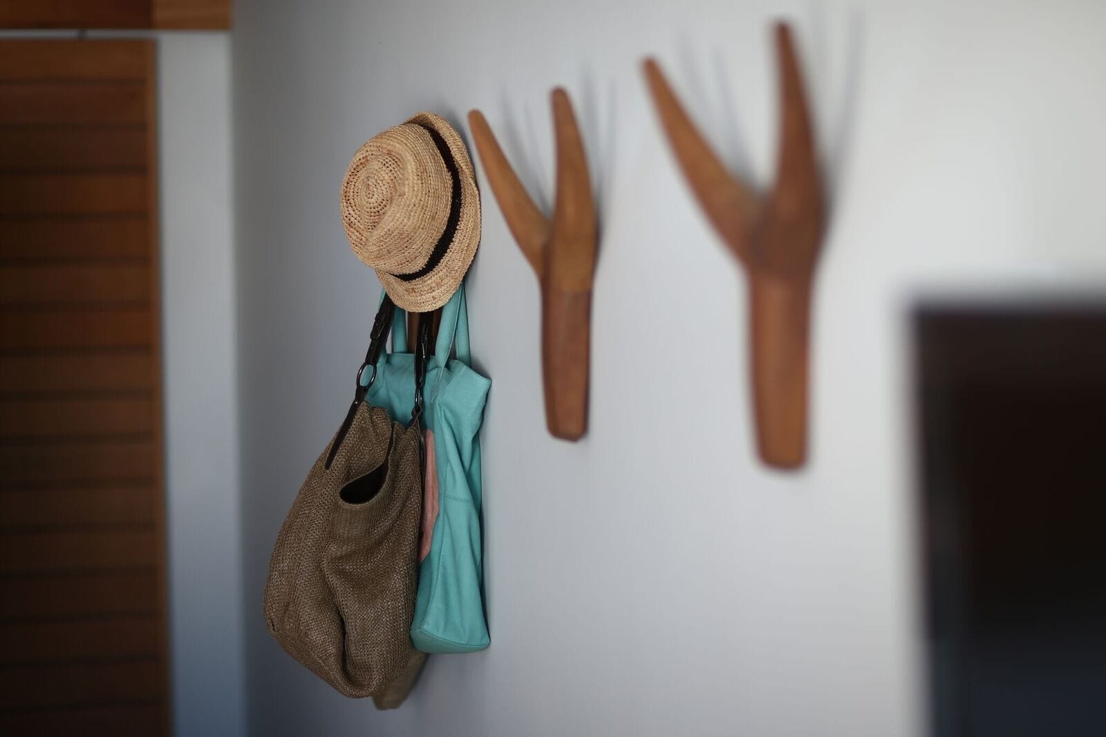A wall with a hat, a pair of gloves, and a brown bag hanging on hooks.