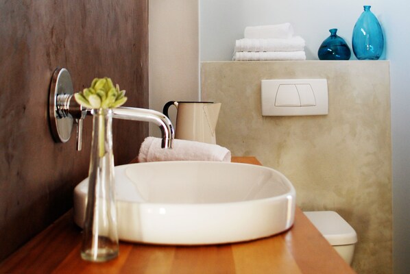 Un baño con lavamanos blanco, grifo, espejo, toallero y retrete.