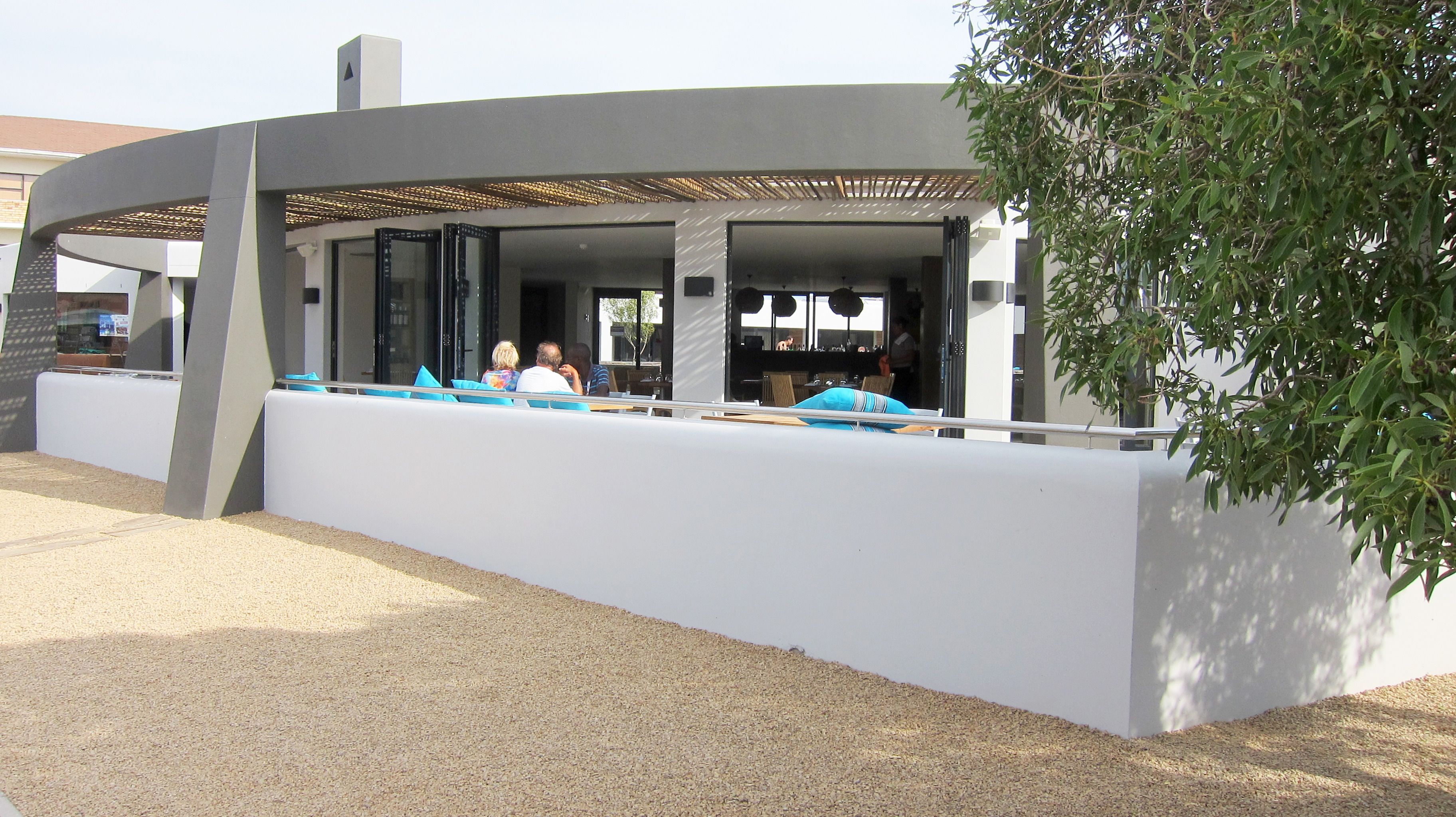 Un espacio de estar al aire libre con diseño moderno, que incluye una pared blanca y cojines azules.