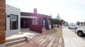 A modern building with a glass storefront, a wooden facade, and a gravel pathway leading to the entrance. - Windtown Lagoon Hotel (Langebaan)