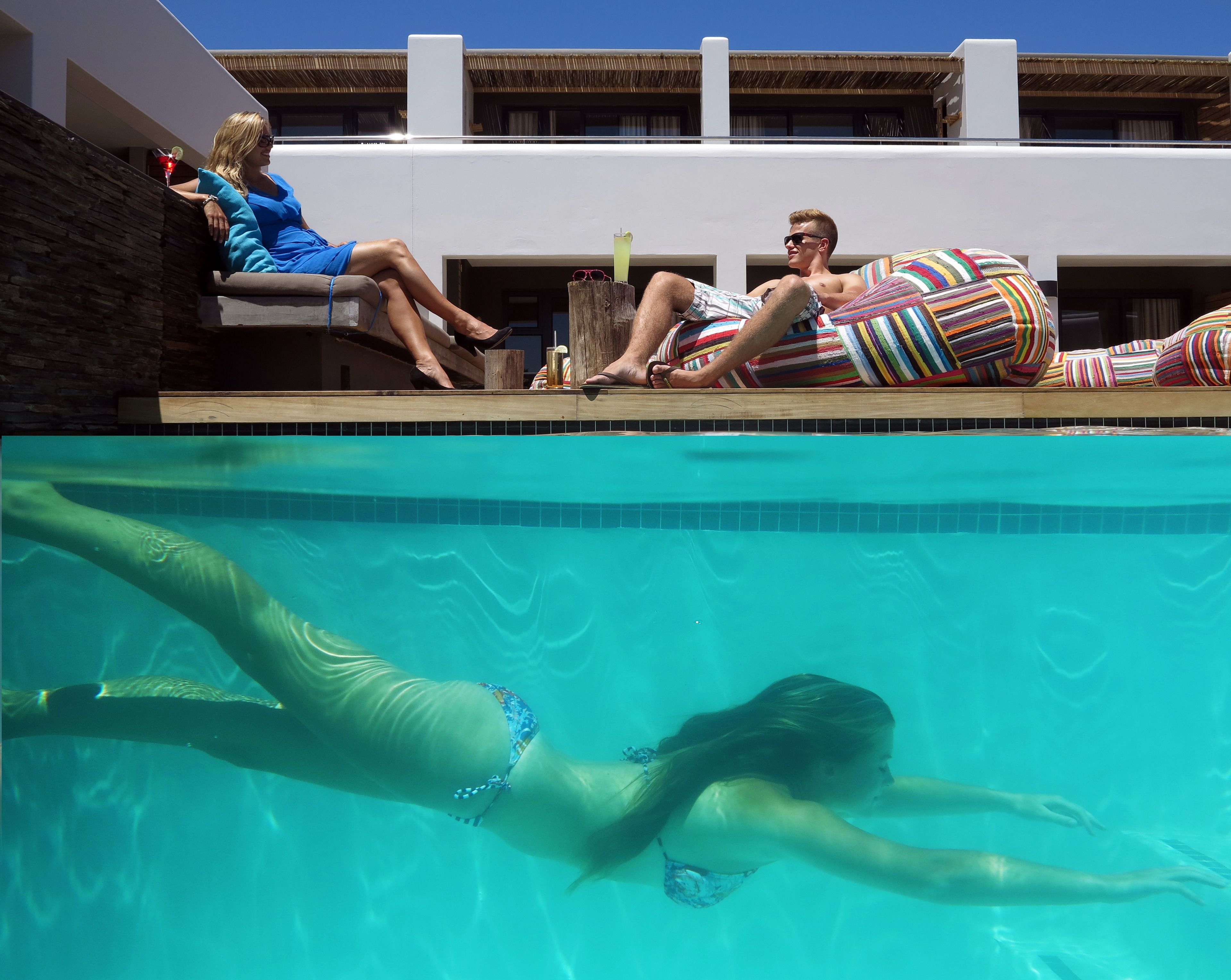 A poolside area with a clear view of the pool, lounge chairs, and a person swimming.