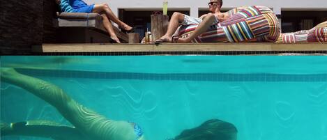 Zona junto a la piscina con vista despejada, sillas de descanso y una persona nadando.