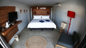 A bedroom with a bed, a television, a chair, a lamp, and a small table. - Windtown Lagoon Hotel (Langebaan)