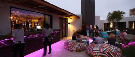 An outdoor seating area with colorful bean bags, a bar with ambient lighting, and a modern building facade.