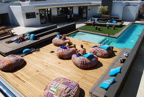 Un área de piscina en la azotea con sillones reclinables y pufs.