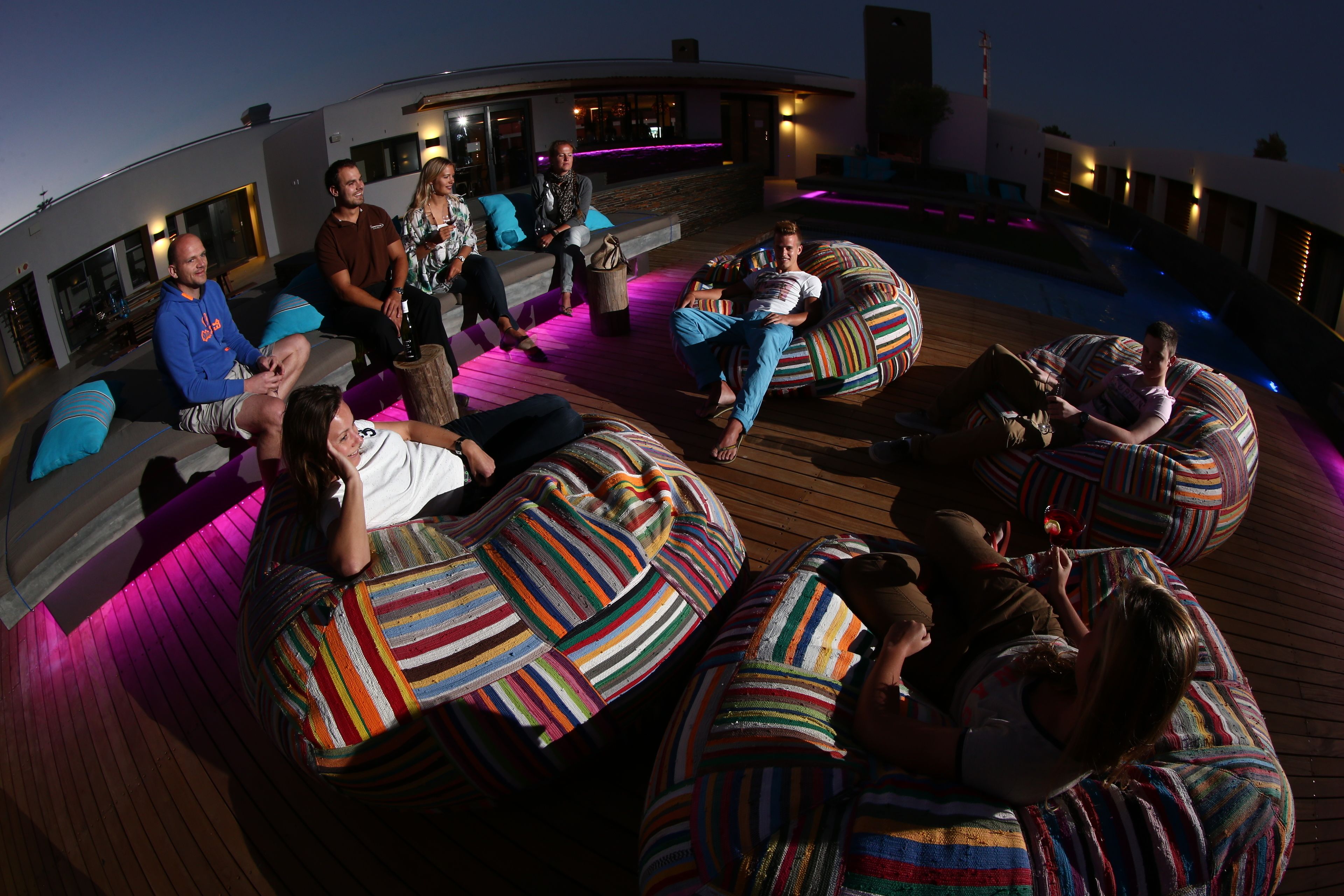 En takterrass med en avslappnad loungeyta, flera sittpuffar och olika sittalternativ, en pool och en modern arkitektonisk design.