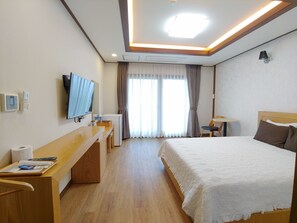A hotel room with a bed, a desk with a chair, a television, and a window with curtains. - Fellisia Hotel (Seogwipo)