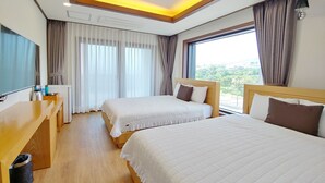 A hotel room with two beds, a desk, a TV, and a large window with curtains. - Fellisia Hotel (Seogwipo)