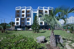 A multi-story building with balconies, surrounded by a landscaped garden with palm trees and rocks. - Fellisia Hotel (Seogwipo)