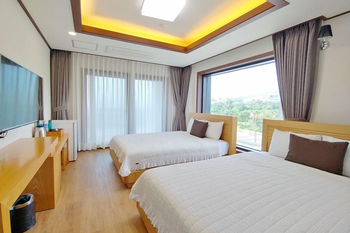A hotel room with two beds, a desk, a TV, and a window with curtains.