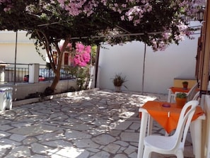 An outdoor patio with stone flooring, white chairs, and orange tablecloths.