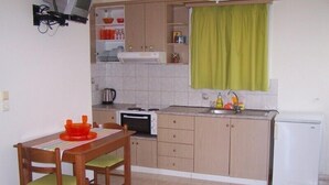 A compact kitchen with a dining area, including a table, chairs, a microwave, a stove, and a sink. - Villa Romantza (Kefalonia)