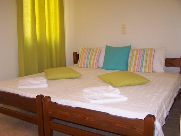 Una cama bien tendida con estructura de madera, ropa de cama blanca y dos almohadas verdes.