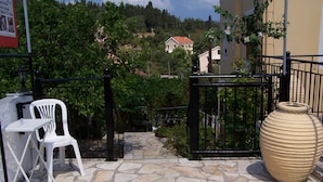 A stone-paved outdoor area with a white plastic chair and a large beige vase. - Villa Romantza (Kefalonia)