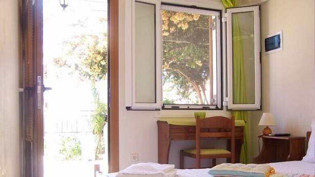 A bedroom with a bed, a desk, and a chair. There is a window with curtains, a lamp, and a wall-mounted TV. - Villa Romantza (Kefalonia)