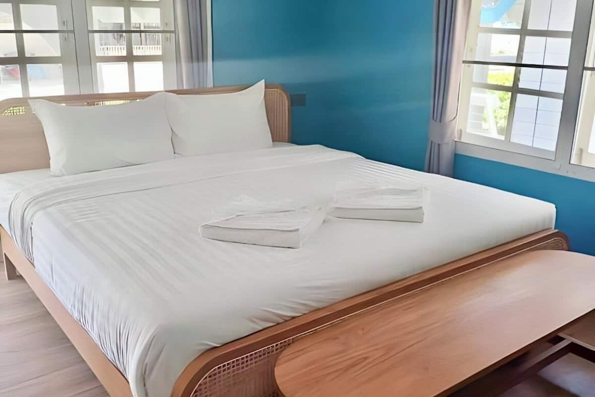 A neatly made bed with white linens and pillows, a wooden bench at the foot of the bed, and a window with curtains.