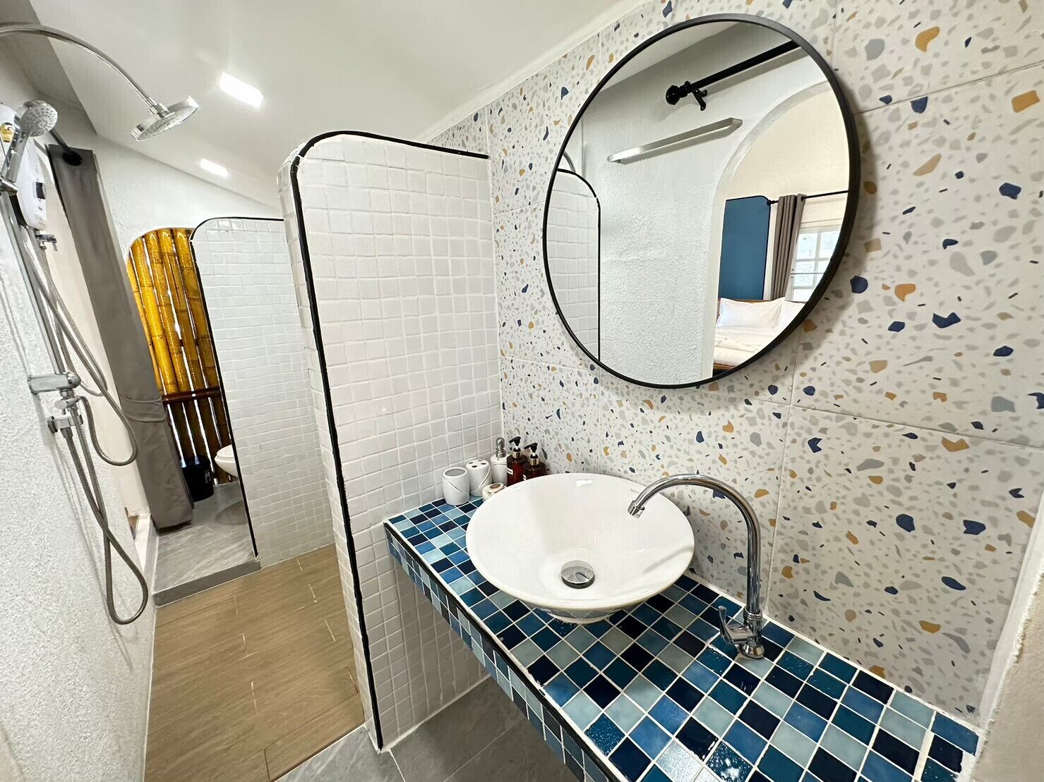 Une salle de bain avec un lavabo blanc, des carreaux de mosaïque bleus, un miroir rond et un espace douche.