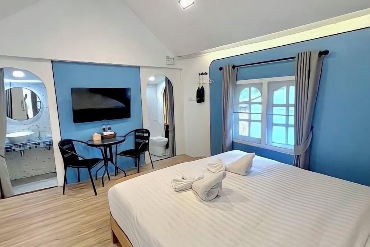 Una habitación de hotel con cama, televisor, escritorio con silla y ventana con cortinas.
