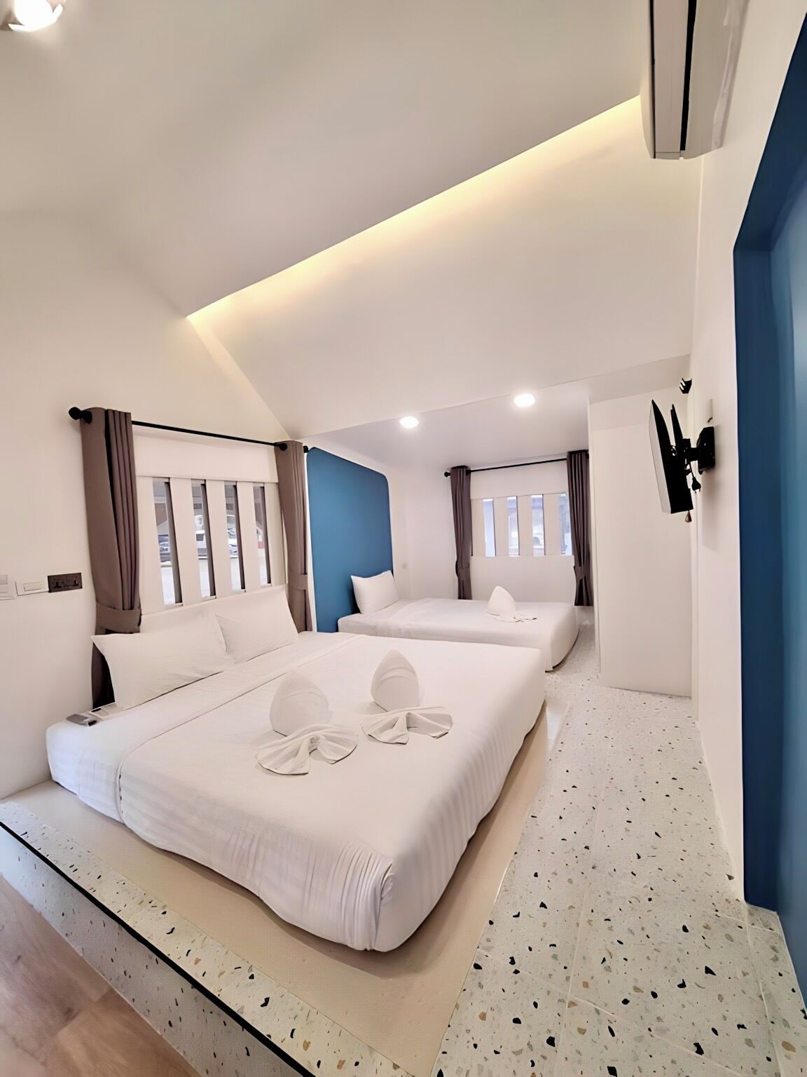 Una habitación de hotel moderna con dos camas, una pared de acento azul y un ventanal con cortinas.