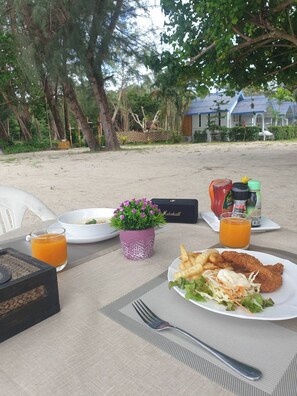 Een gedekte tafel met een maaltijd, inclusief salade, friet en gebraden kip, samen met sauzen en een drankje.