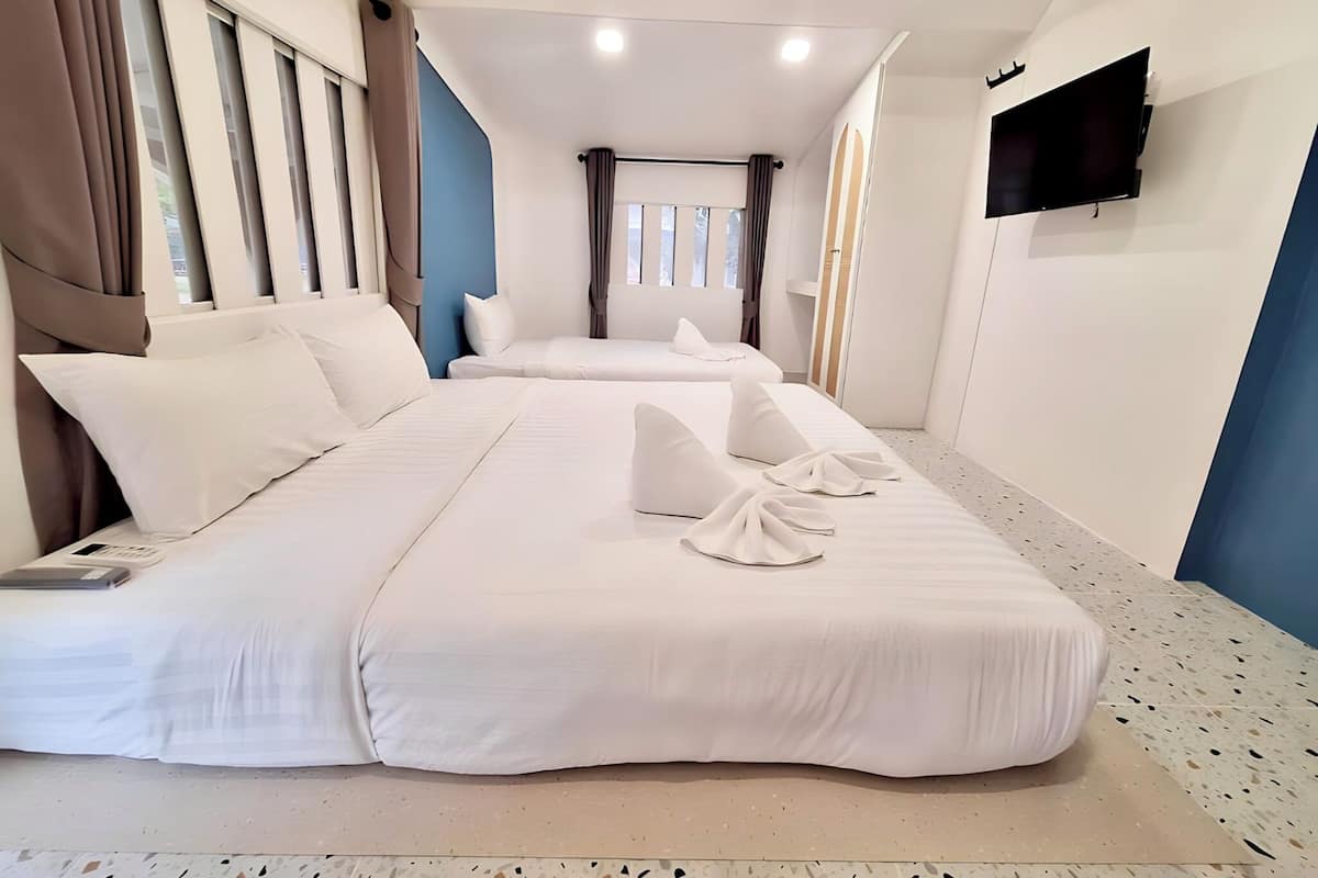 A hotel room with two beds, a flat-screen TV mounted on the wall, and a window with curtains.
