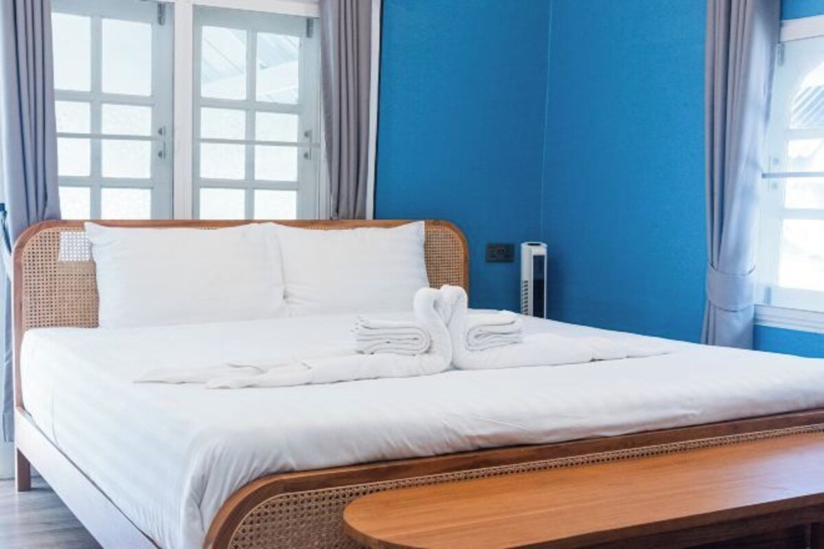 A neatly made bed with white linens and towels, a wooden headboard, and a bedside table.